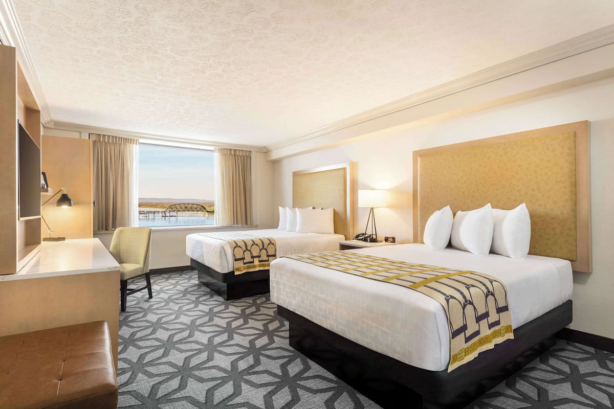A hotel room with two beds, a desk, a chair, a TV, and a large window with a view.