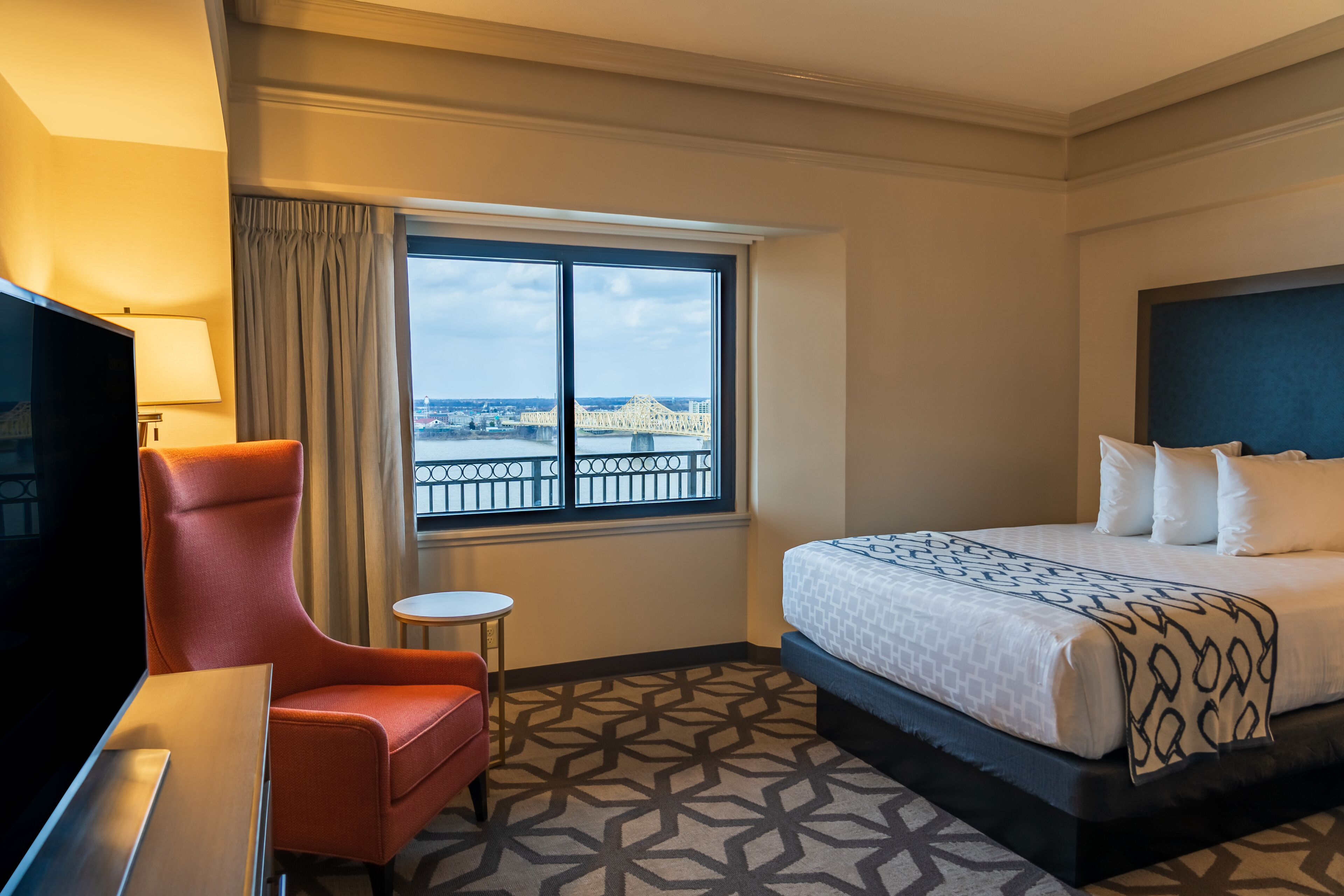 Une chambre d’hôtel avec un grand lit, une télévision, une petite table et une fenêtre donnant sur un pont.
