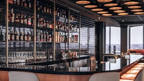 A modern bar with a long counter, multiple shelves of liquor bottles, and cushioned bar stools.