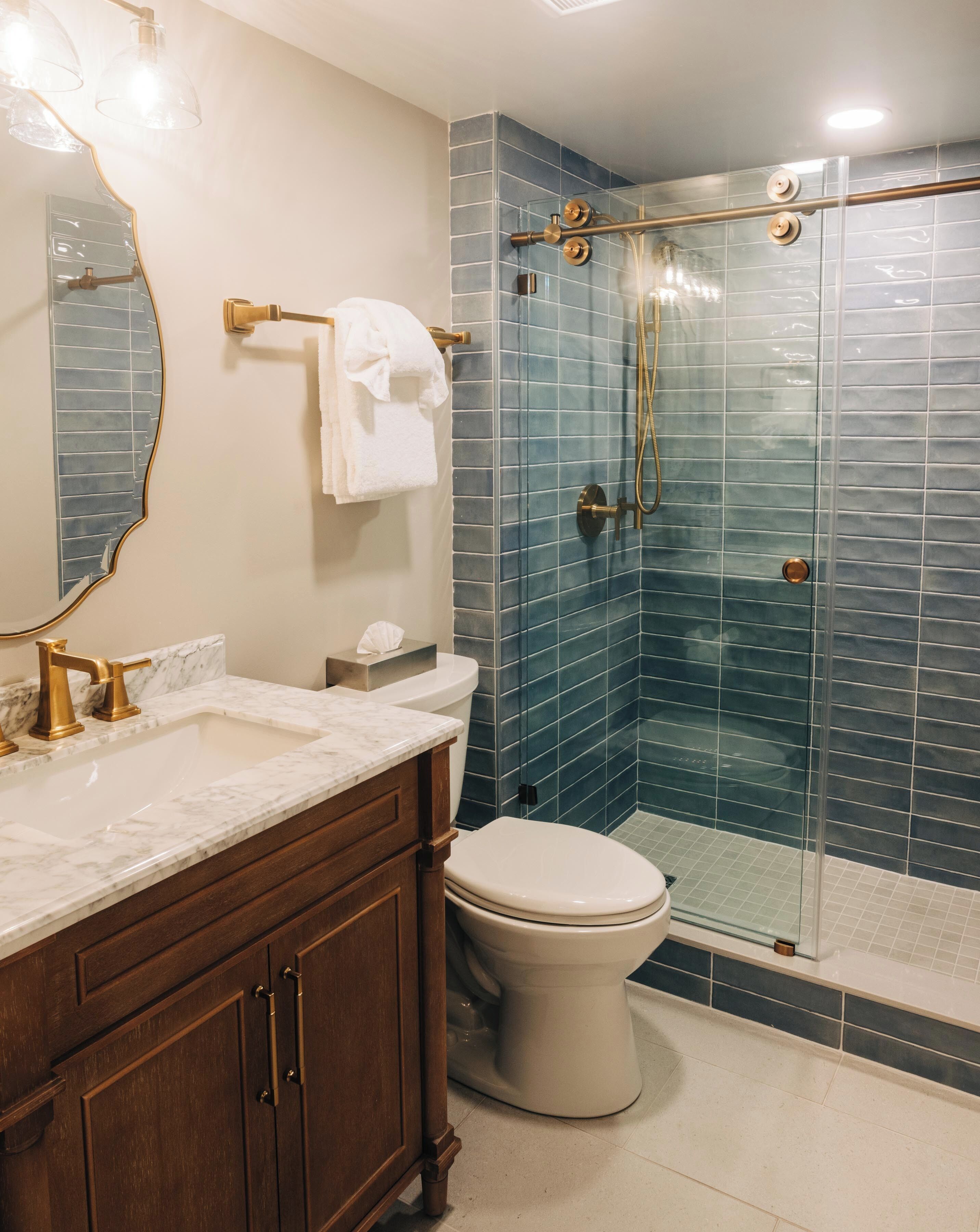A bathroom with a marble sink, a toilet, a glass shower enclosure, and a mirror with a gold frame.