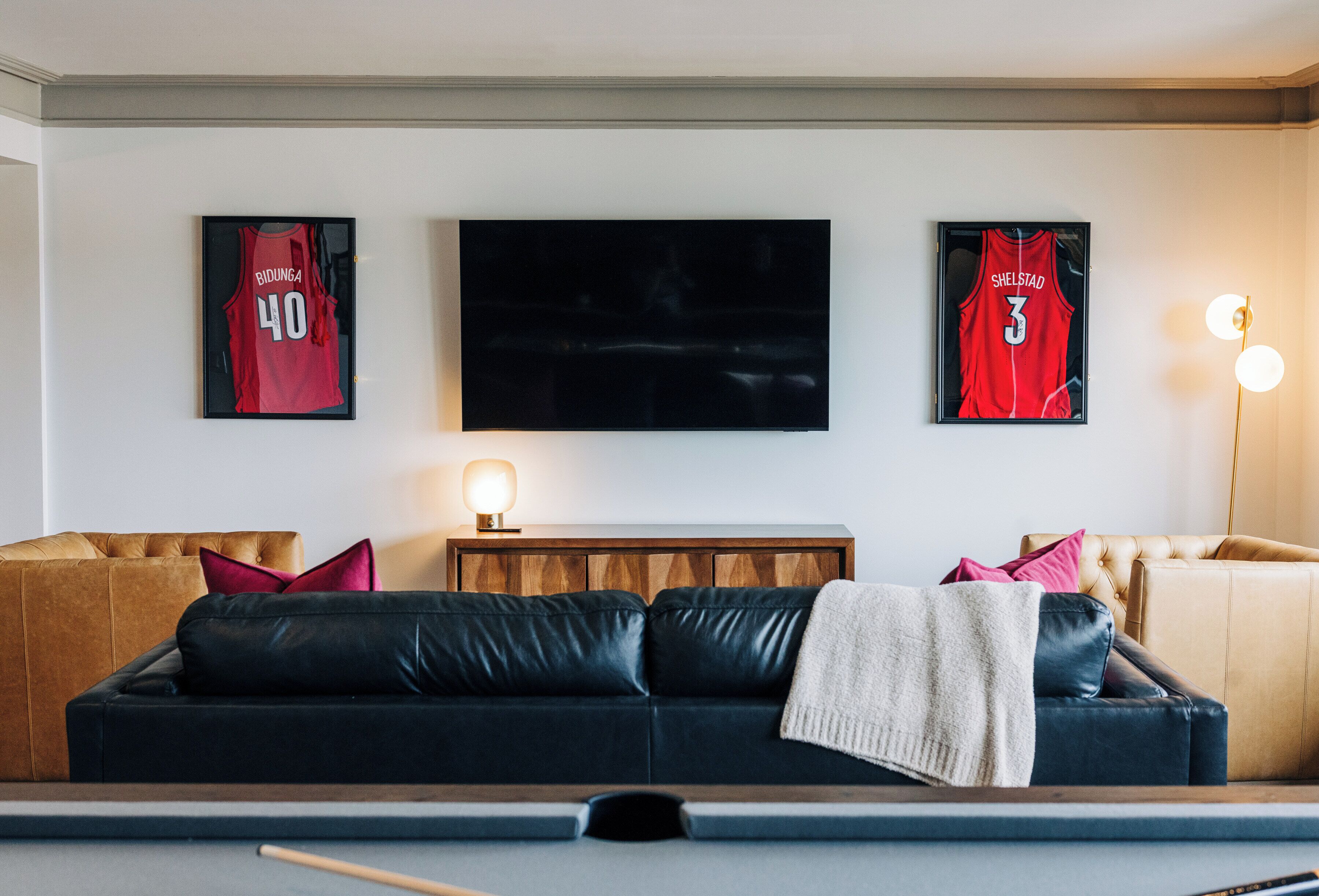 A living room with a black leather sofa, a wooden coffee table, and a television mounted on the wall.