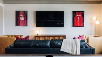 A living room with a black leather sofa, a wooden coffee table, and a television mounted on the wall.