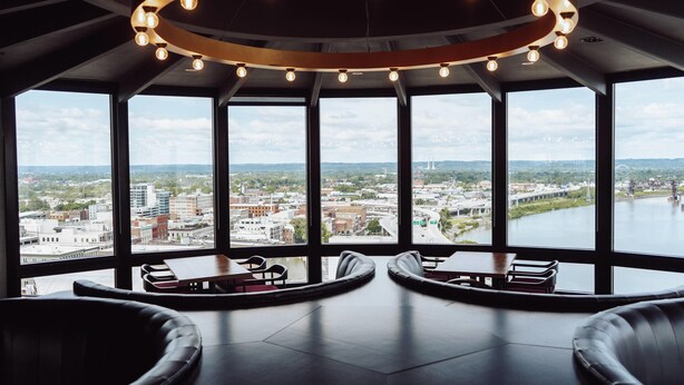 A modern interior with large windows offering a city view, a circular light fixture, and leather seating.