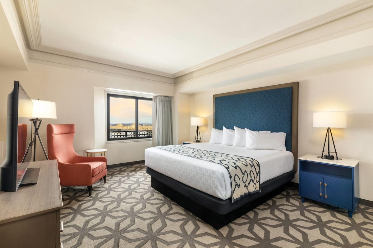 A hotel room with a large bed, a desk, a chair, a nightstand, and a window with a view.