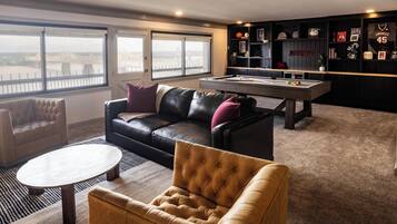 A modern living room with a pool table, leather sofas, and a view of a cityscape through large windows.