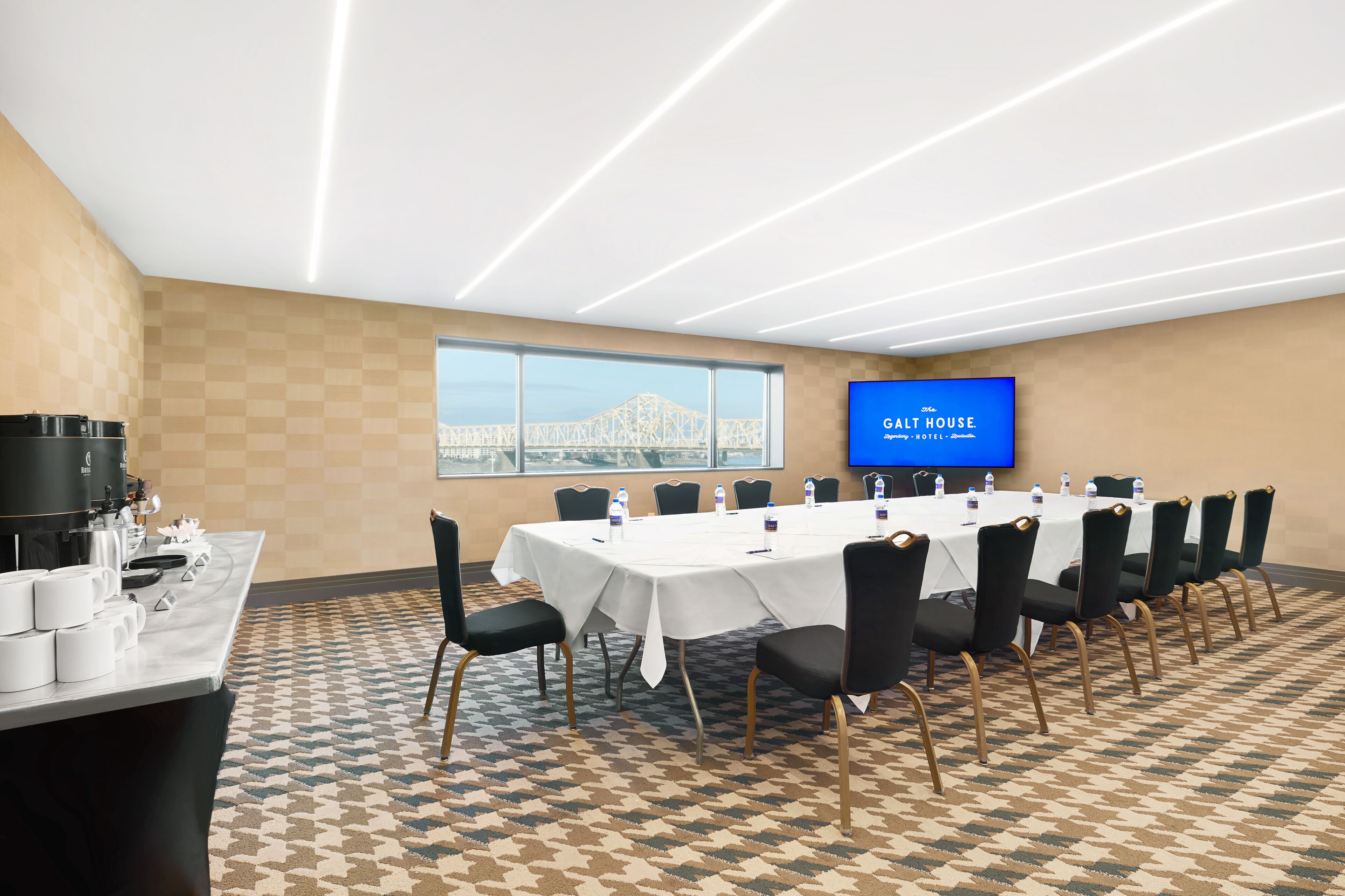 Uma sala de conferências com uma mesa comprida, cadeiras, um espaço para café e uma tela de TV exibindo "GALT HOUSE".