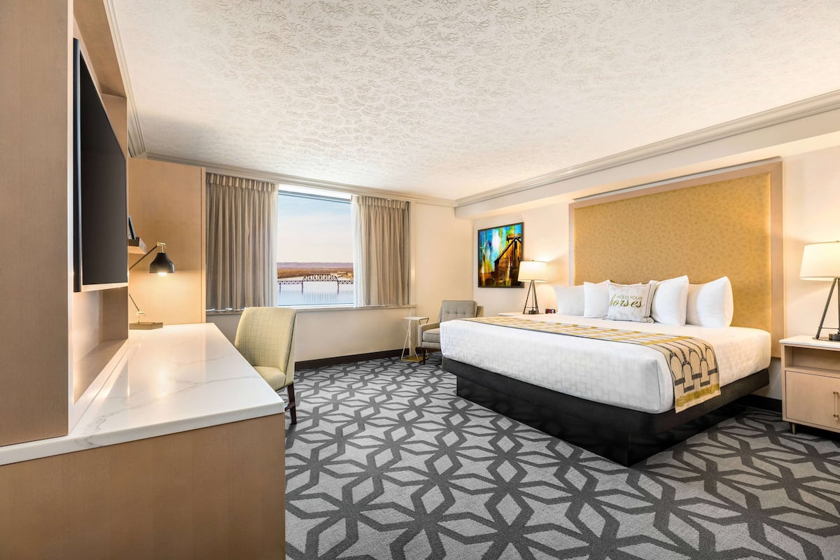 A hotel room with a large bed, a desk, a chair, a TV, and a painting on the wall.