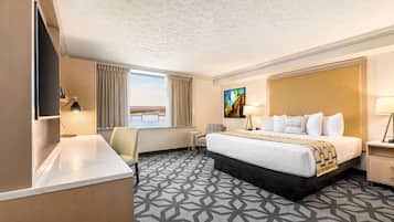 A hotel room with a large bed, a desk, a chair, a TV, and a painting on the wall.