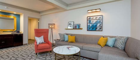 A living room with a sofa, armchair, coffee table, and artwork on the wall.