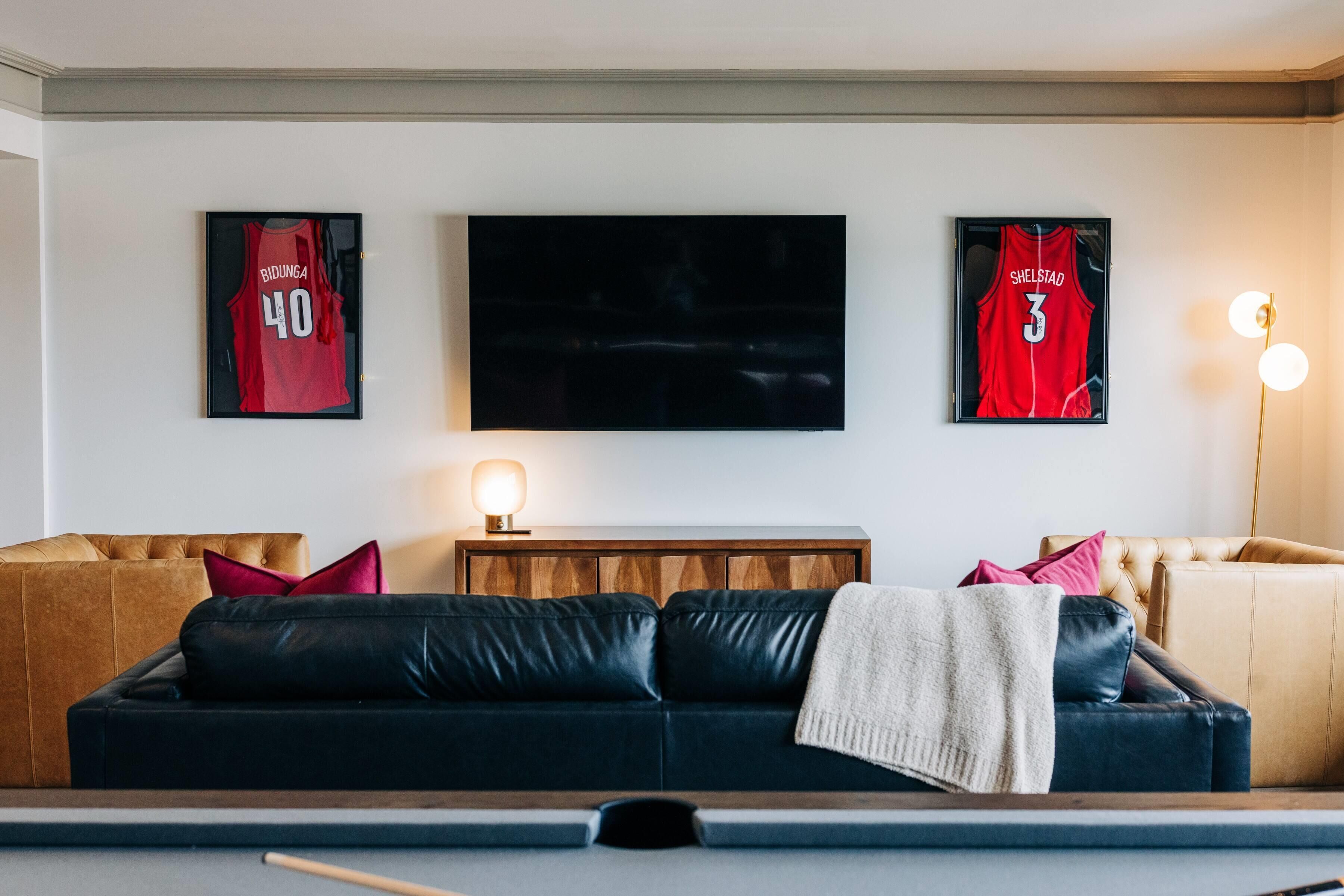 Una sala de estar con mesa de billar, dos camisetas enmarcadas, un televisor de pantalla plana y un mueble de madera.