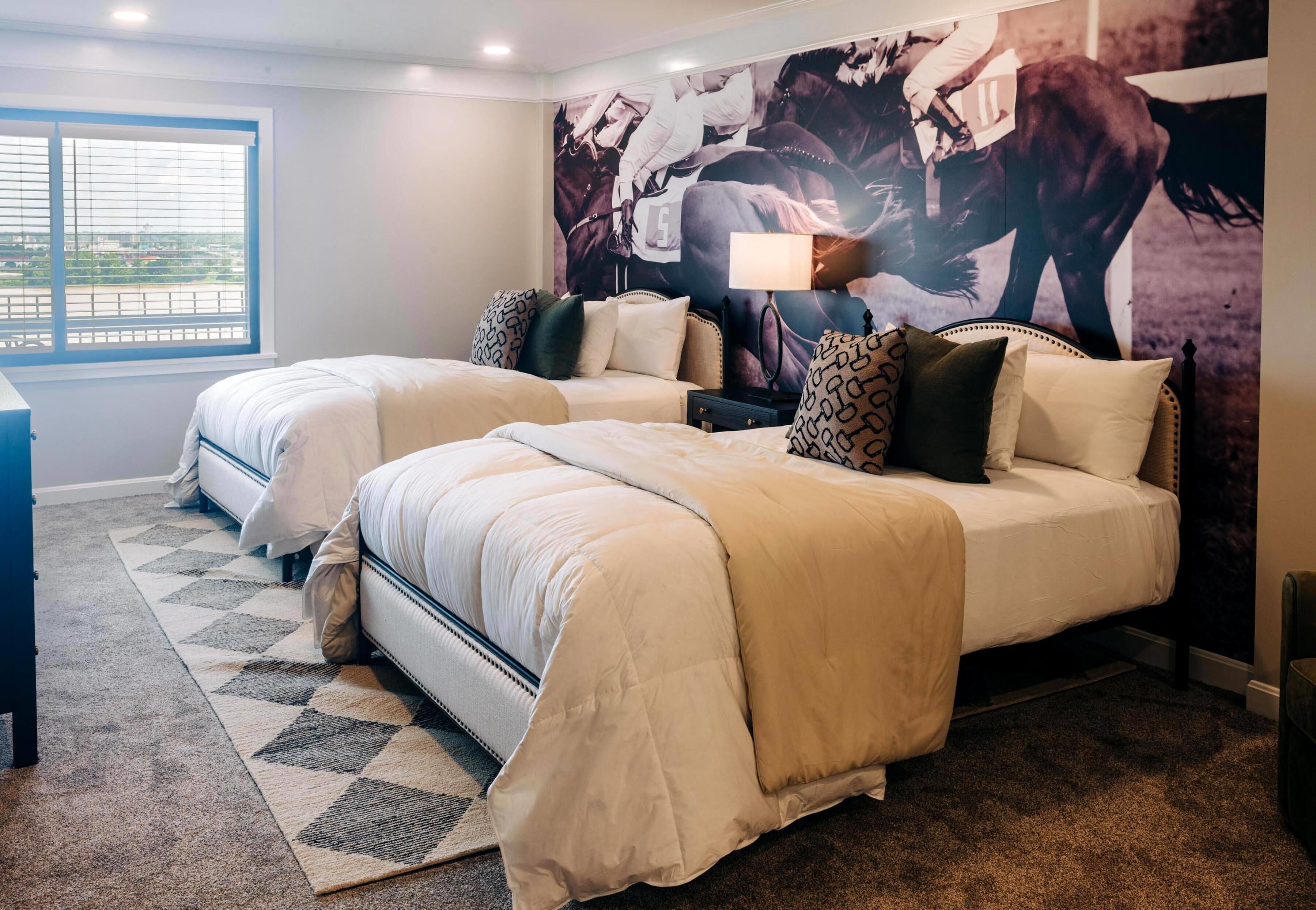A hotel room with two beds, a large window, a patterned rug, and a wall mural.