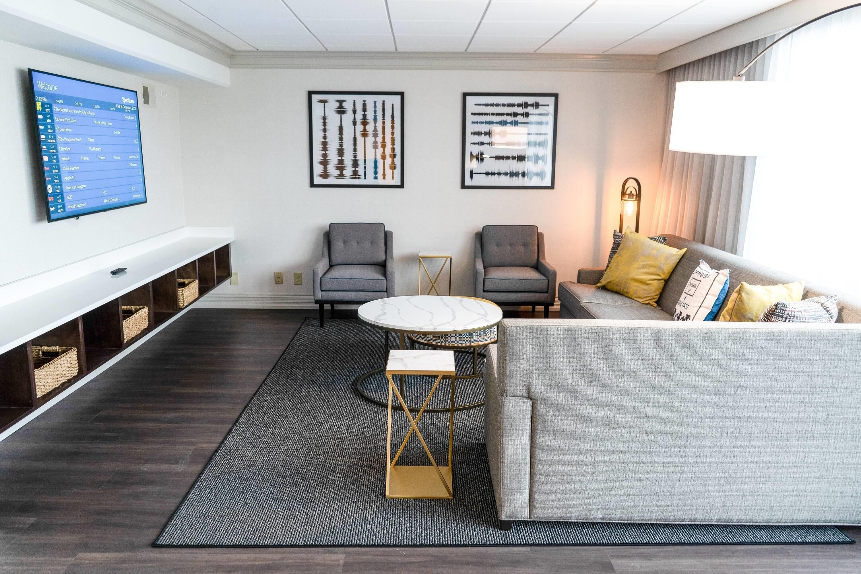 Een moderne woonkamer met een flatscreen televisie, twee fauteuils, een bank, een salontafel en kunstwerken in lijsten aan de muur.