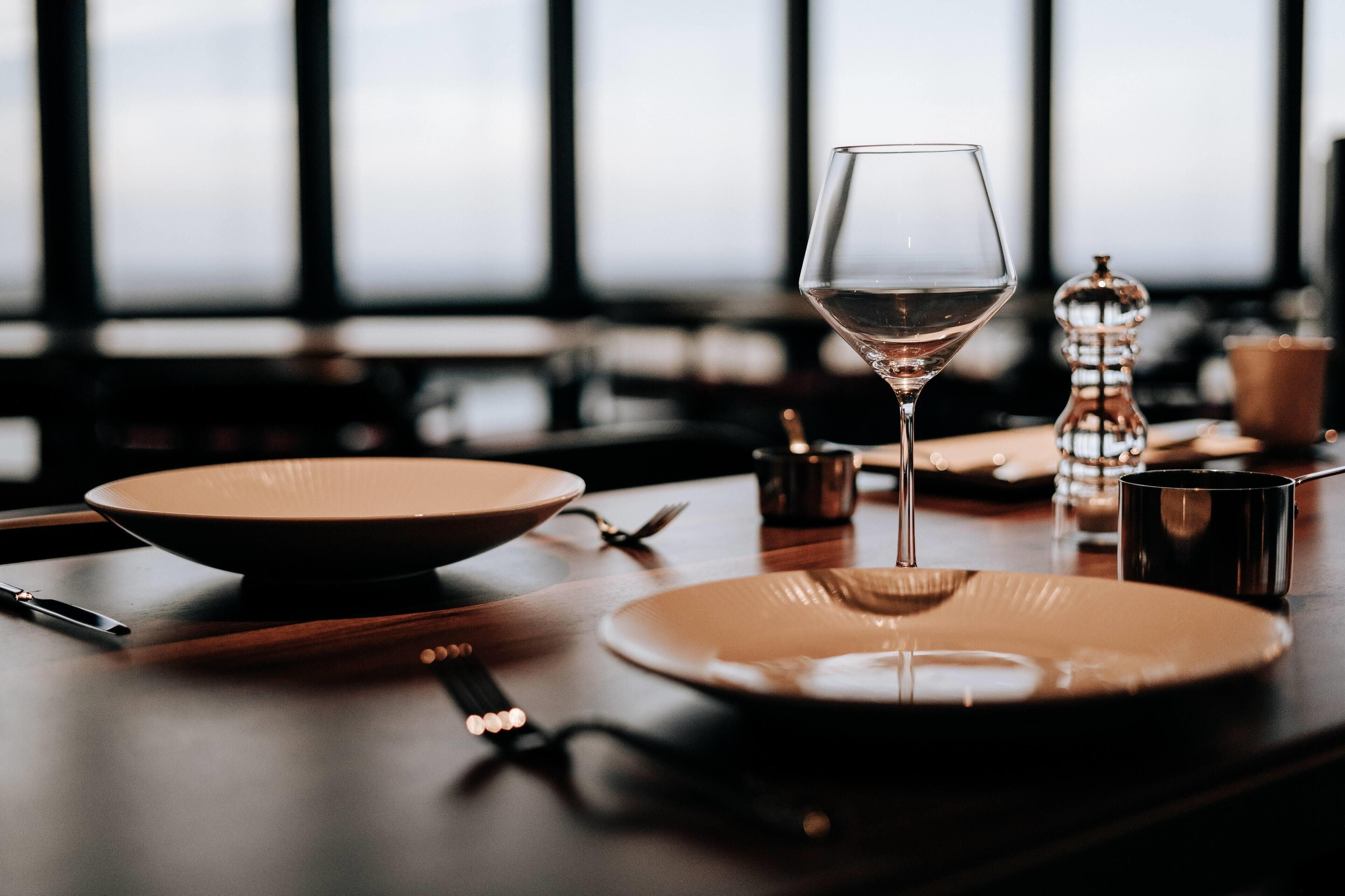 Una mesa servida con una copa de vino, platos, cubiertos y salero y pimentero.