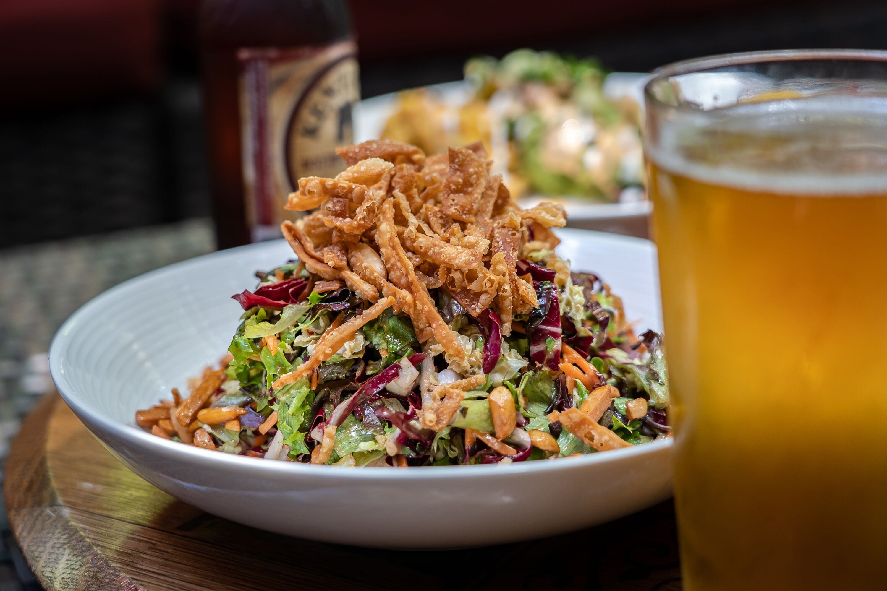 Eine Salatschüssel mit knusprigen Zutaten und ein Glas Bier auf einem Holztisch.