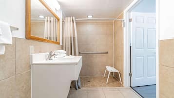 A bathroom with a sink, mirror, shower, and door.