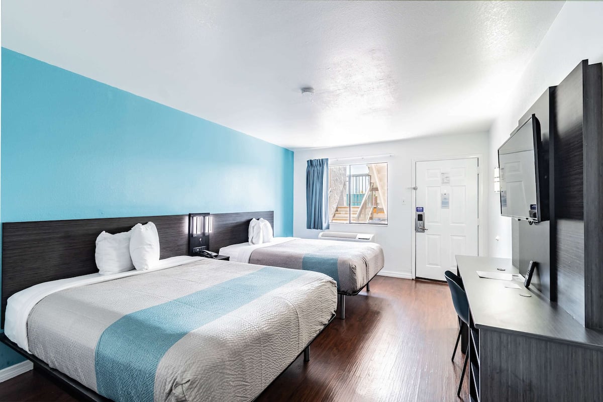 Habitación de hotel con dos camas, un escritorio, un televisor y una ventana con cortinas.