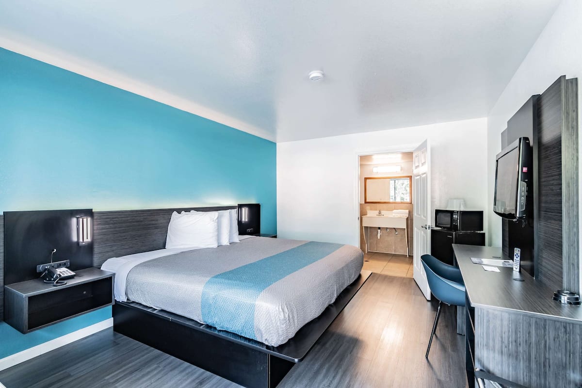 Una habitación de hotel moderna con cama, mesita de noche, televisor y una pequeña zona de escritorio.