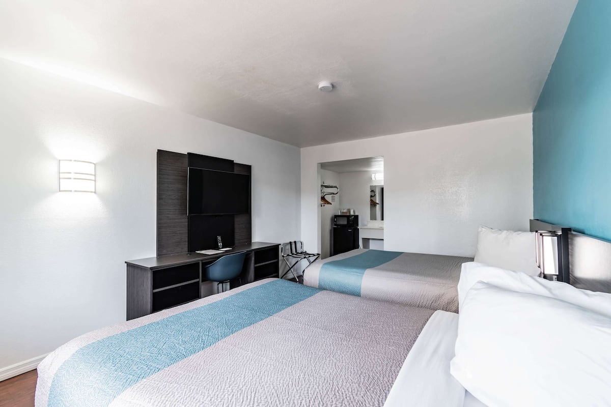 Habitación de hotel con dos camas, un escritorio, una silla y un televisor.