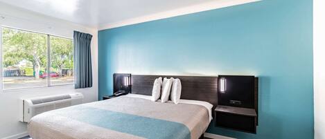 Una habitación de hotel moderna con una cama grande, una mesita de noche, un estante en la pared y una ventana con cortinas.