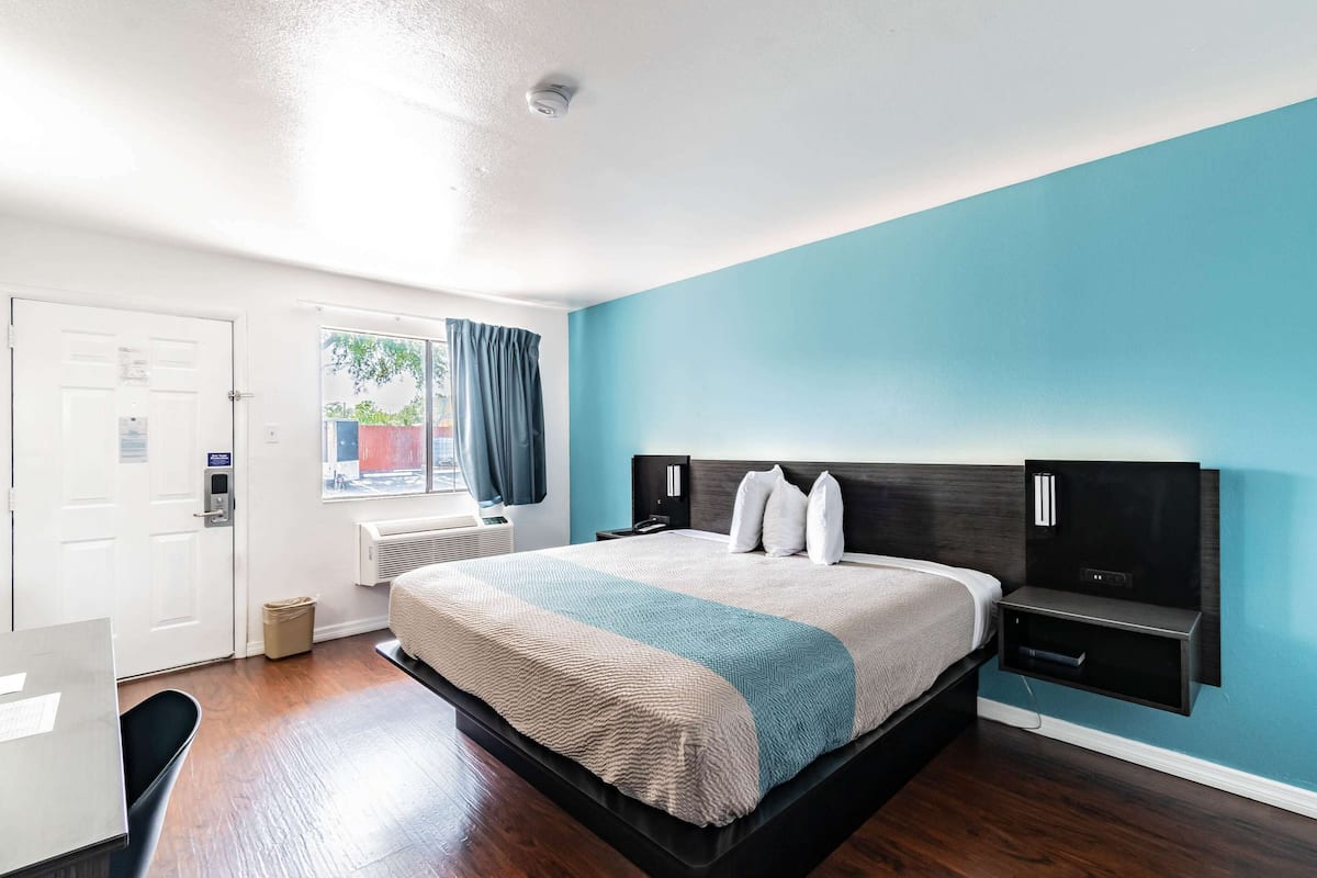 Una habitación de hotel moderna con una cama grande, un escritorio, una ventana con cortinas y un televisor montado en la pared.