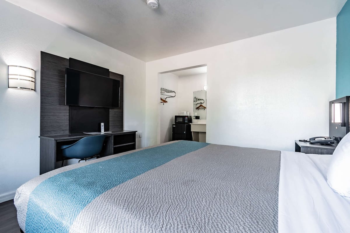 Habitación de hotel con una cama grande, un escritorio con una silla, un televisor de pantalla plana, un microondas y una mesita con un teléfono.