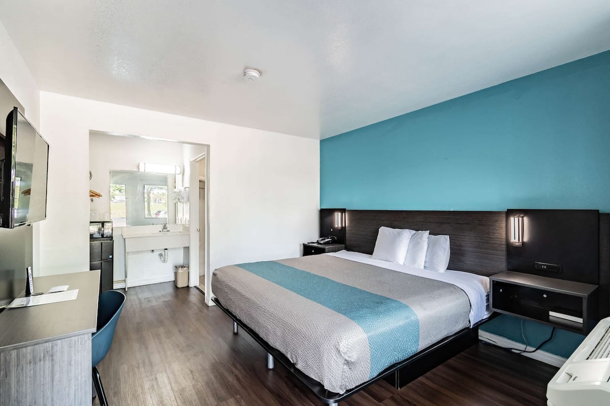 Una habitación de hotel moderna con una cama grande, un escritorio, una silla, un tocador con espejo y un baño.