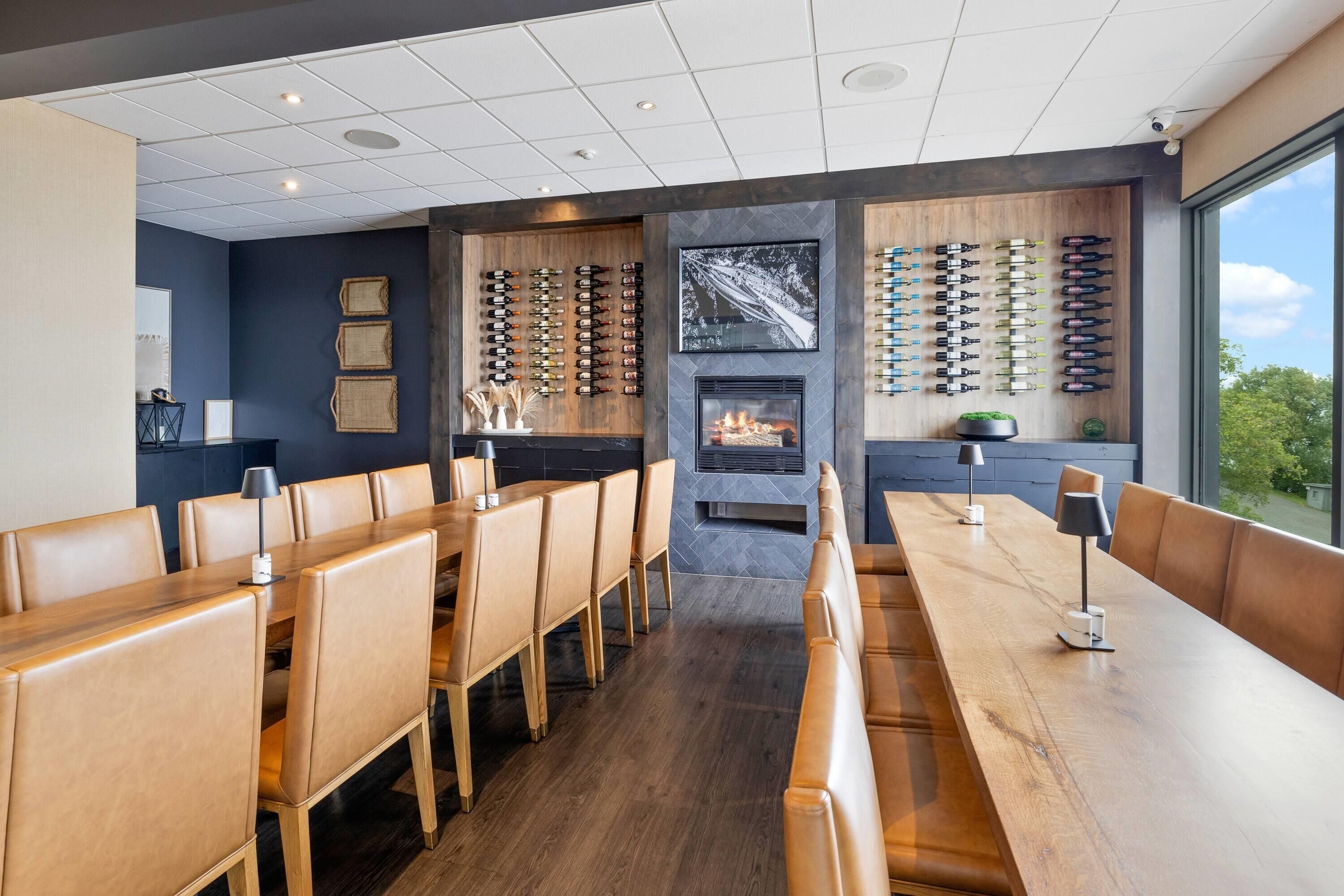 A modern dining area with wooden tables and chairs, a fireplace, and wine racks on the walls.