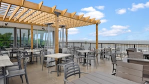 An outdoor dining area with tables and chairs, a wooden pergola, and a view of the sea. - The Jordan Ramada by Wyndham (Lincoln)