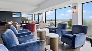 A modern lounge area with large windows, comfortable seating, and a view of the sea. - The Jordan Ramada by Wyndham (Lincoln)