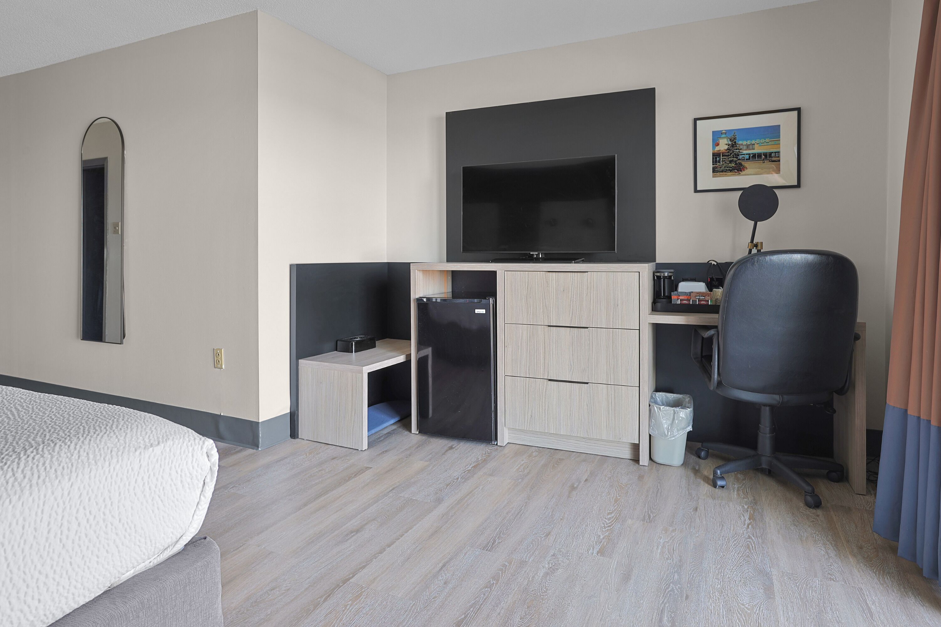 Quarto de hotel com uma cama, escrivaninha com computador, televisão e um pequeno frigorífico.