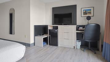 Quarto de hotel com uma cama, escrivaninha com computador, televisão e um pequeno frigorífico.