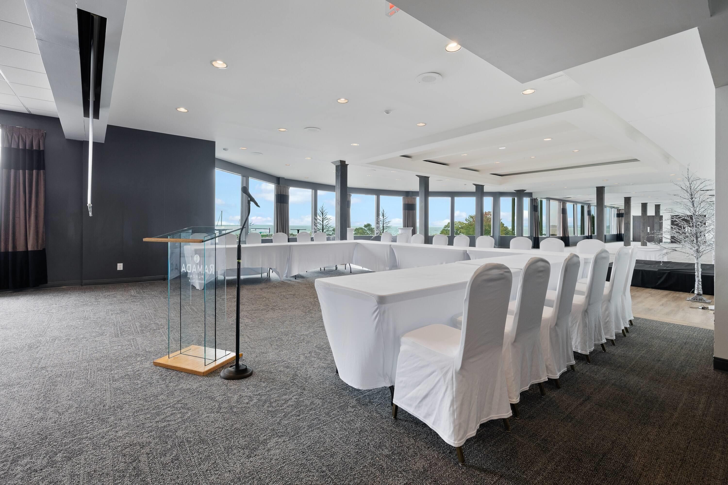 A modern conference room with a long table, white chairs, and large windows offering a view of the outdoors.