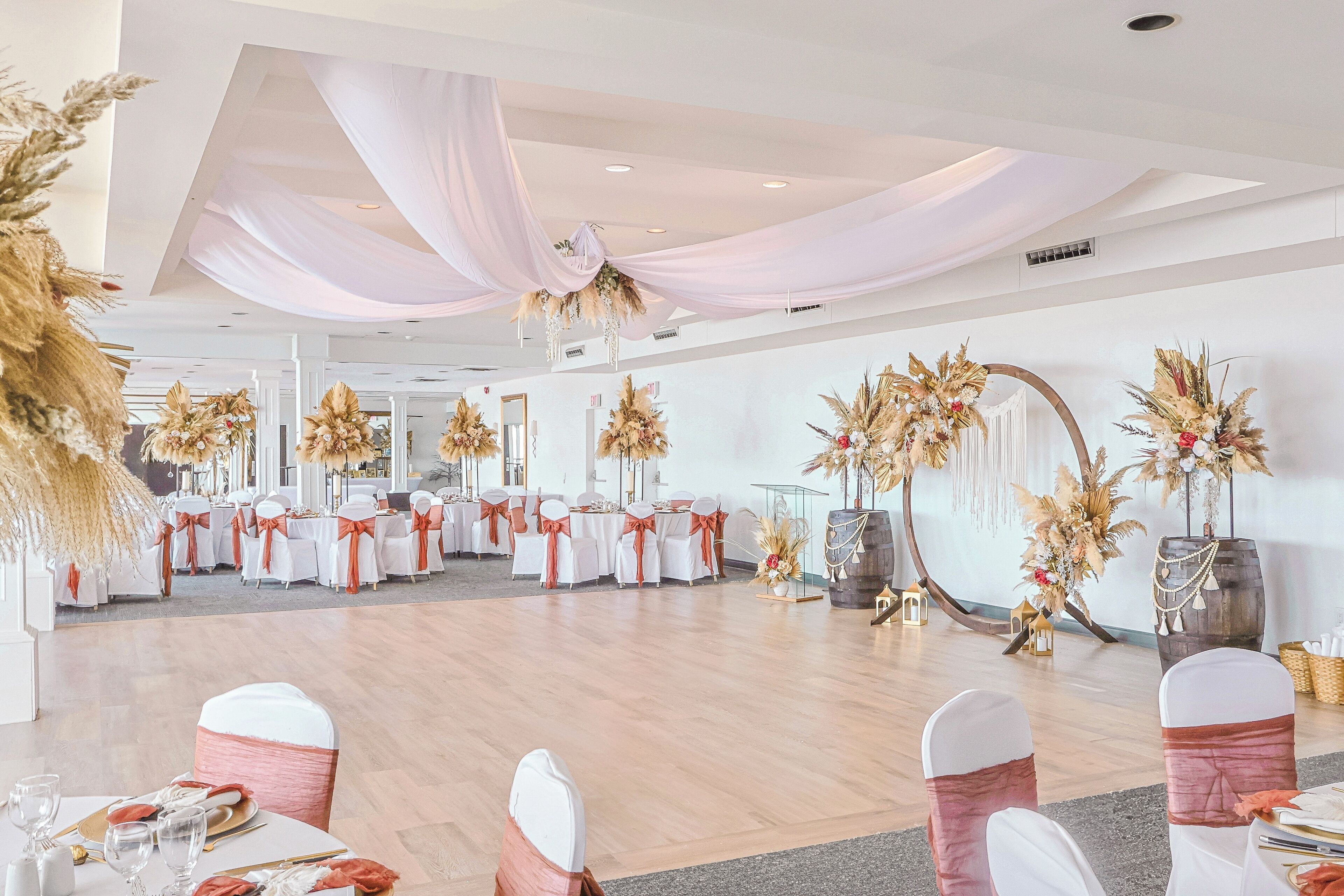 A banquet hall with round tables, white chairs with pink sashes, and floral centerpieces.