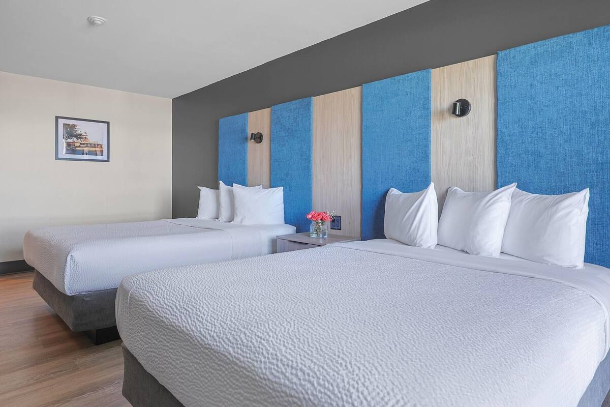 A hotel room with two beds, a nightstand, and a framed picture on the wall.