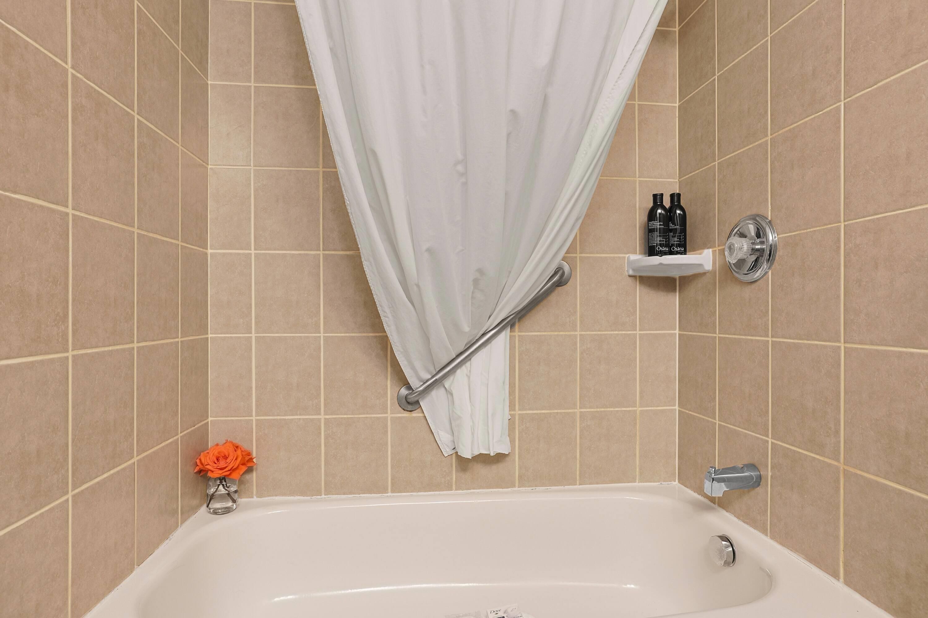 Een badkamer met een bad, douchegordijn, handdoekrek en een plank met toiletartikelen.