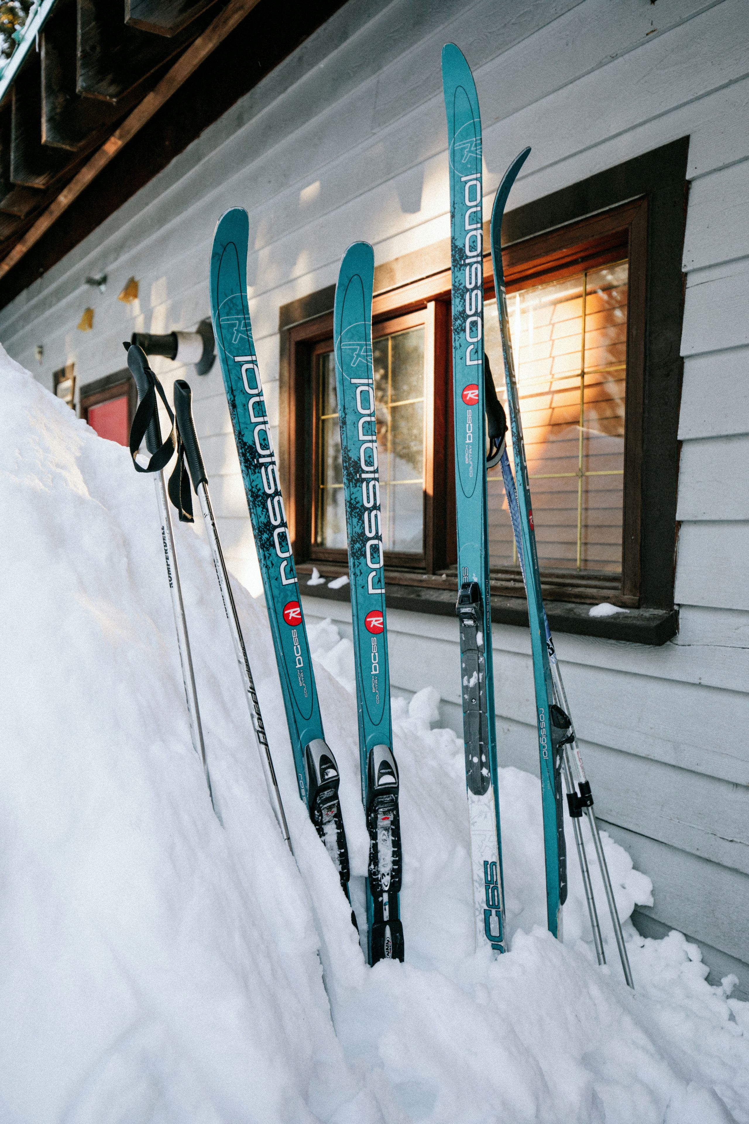 A row of skis leaning against a house with a window.
