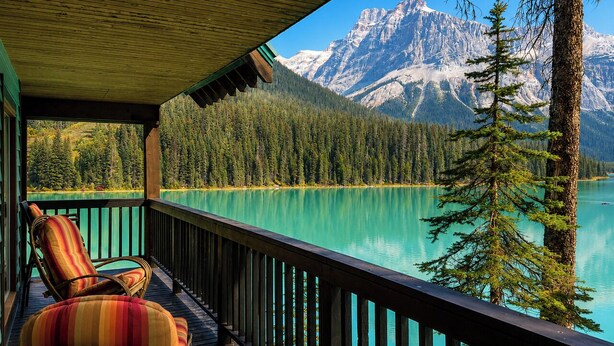 A wooden deck with a view of a turquoise lake and snow-capped mountains. - Emerald Lake Lodge (Field)