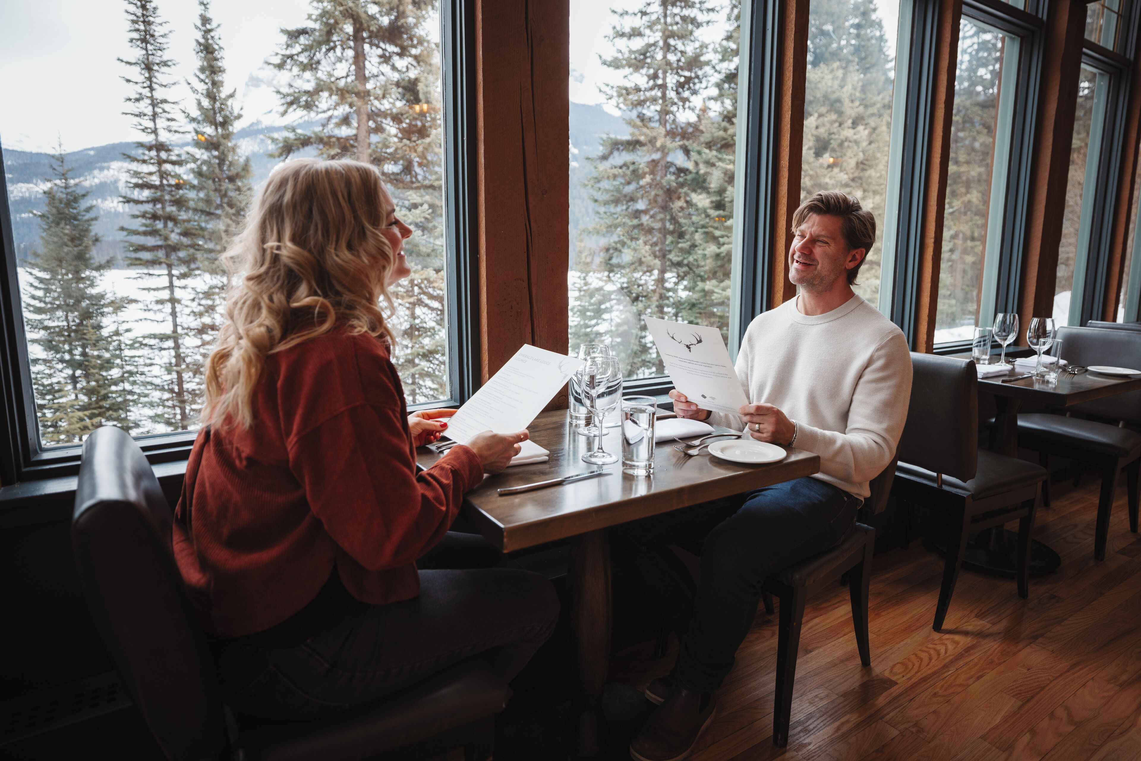 Un comedor con una mesa de madera, sillas y vistas a árboles y montañas a través de amplios ventanales.