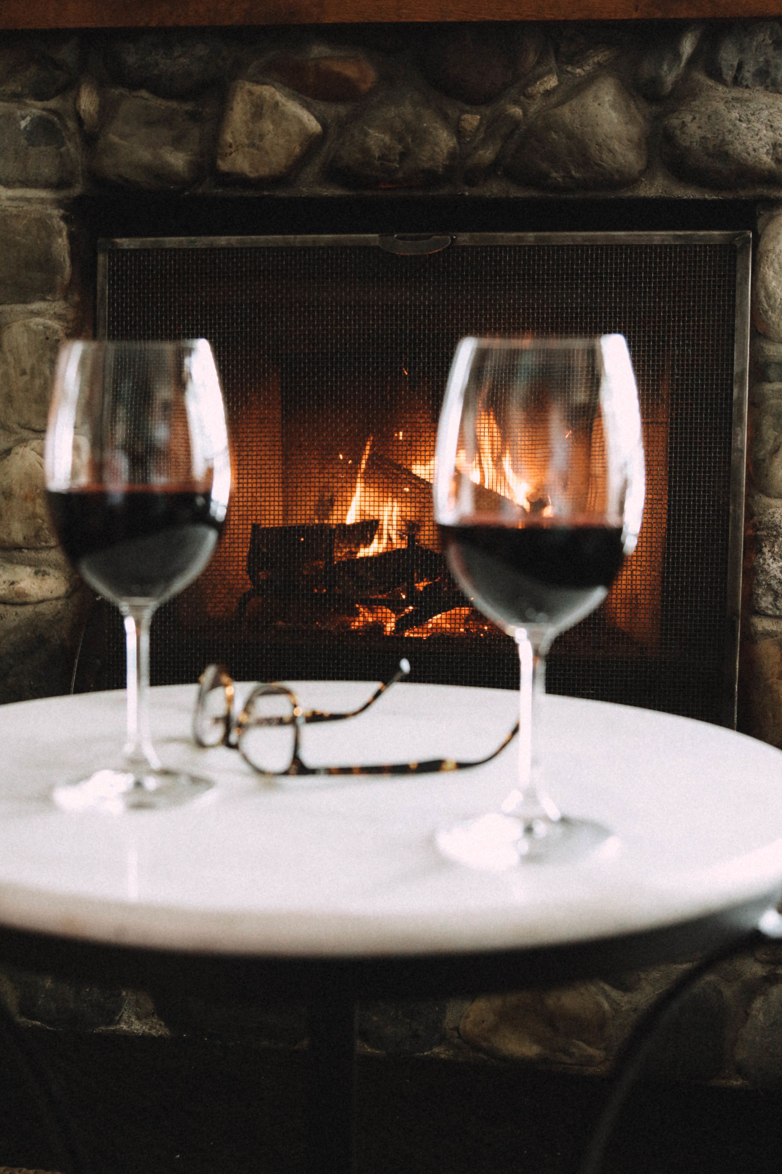 Deux verres à vin sont posés sur une table, avec une cheminée en arrière-plan.