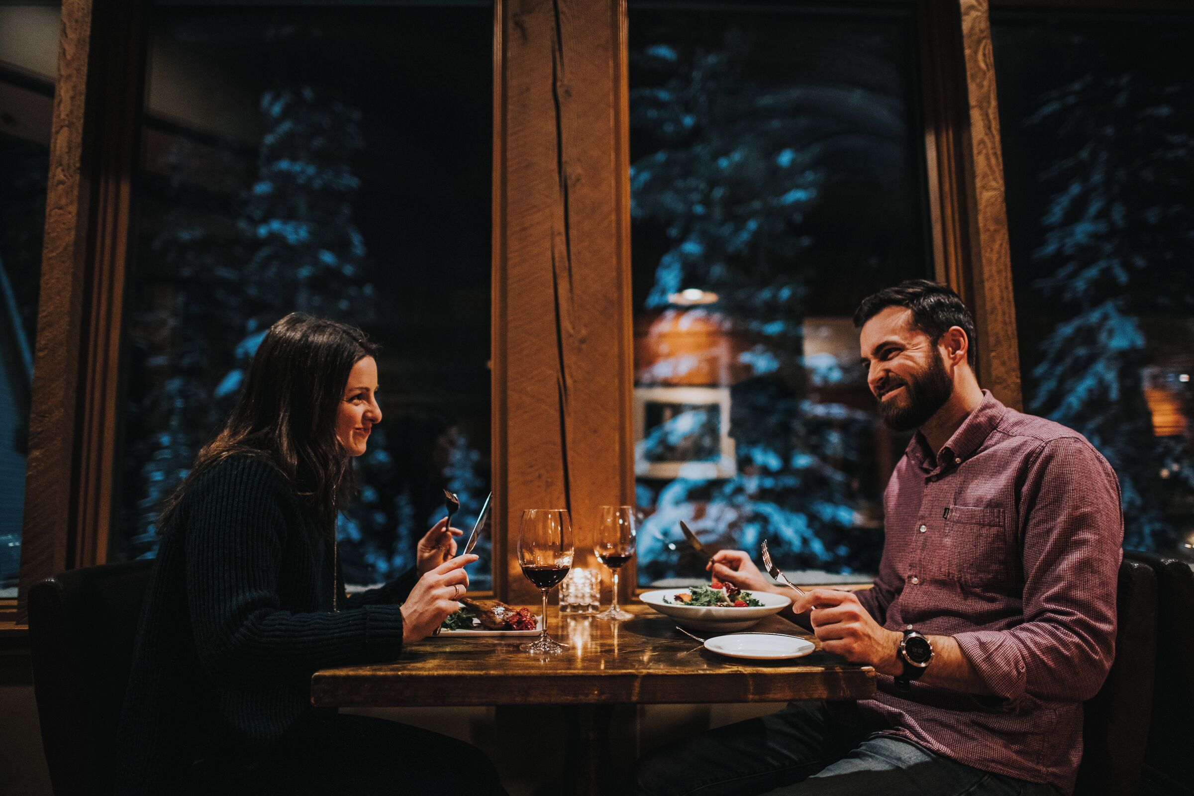 Deux personnes sont assises à une table, devant des verres à vin et des assiettes remplies de nourriture.