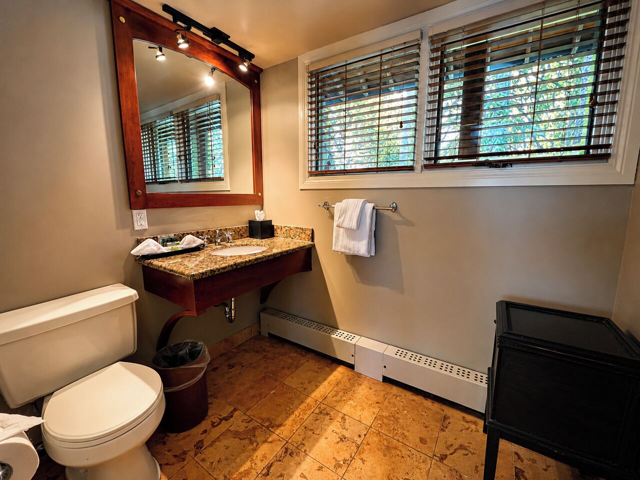 A bathroom with a toilet, sink, mirror, window with blinds, and a radiator.