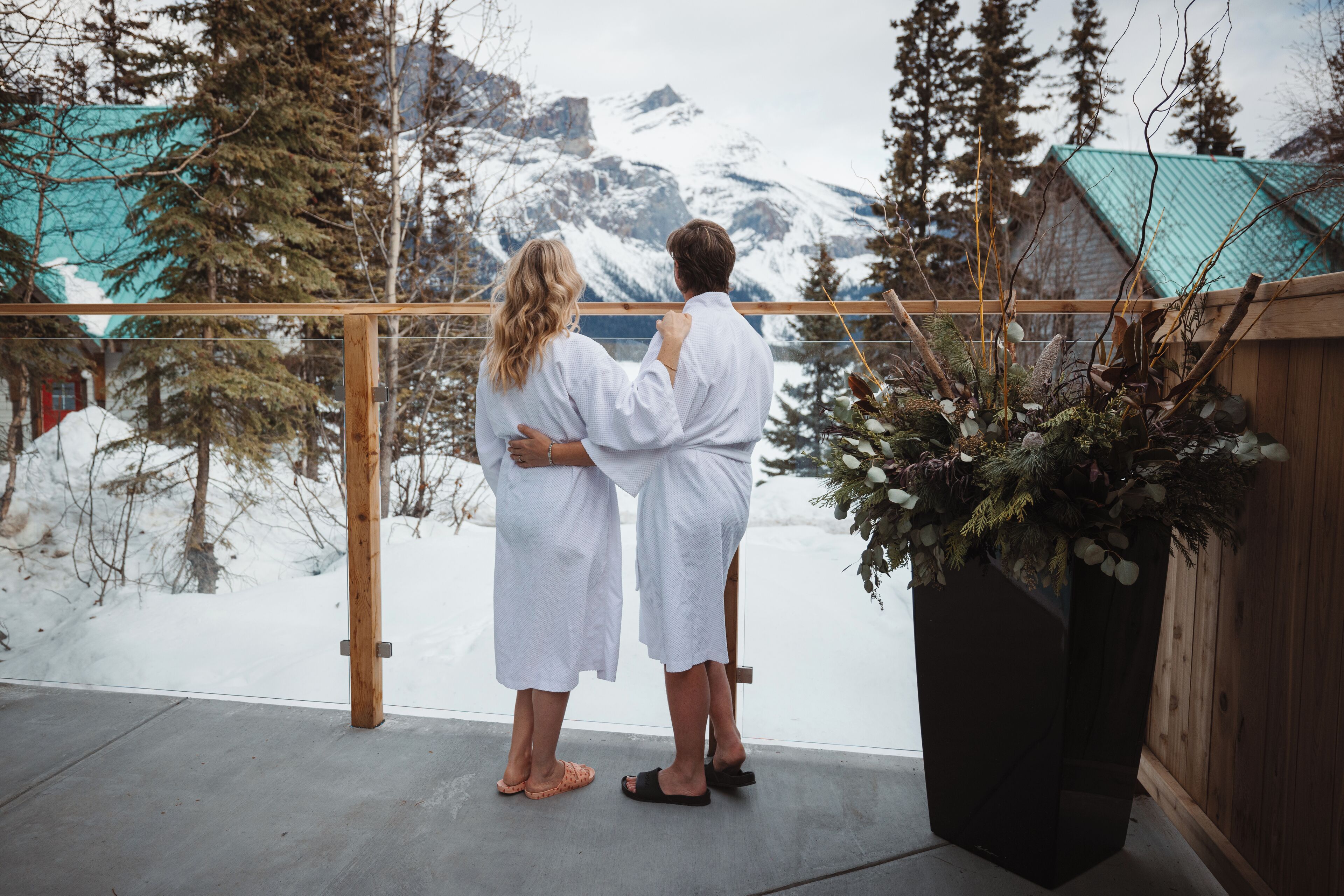 Una pareja está de pie en un balcón con vista a un paisaje montañoso nevado.