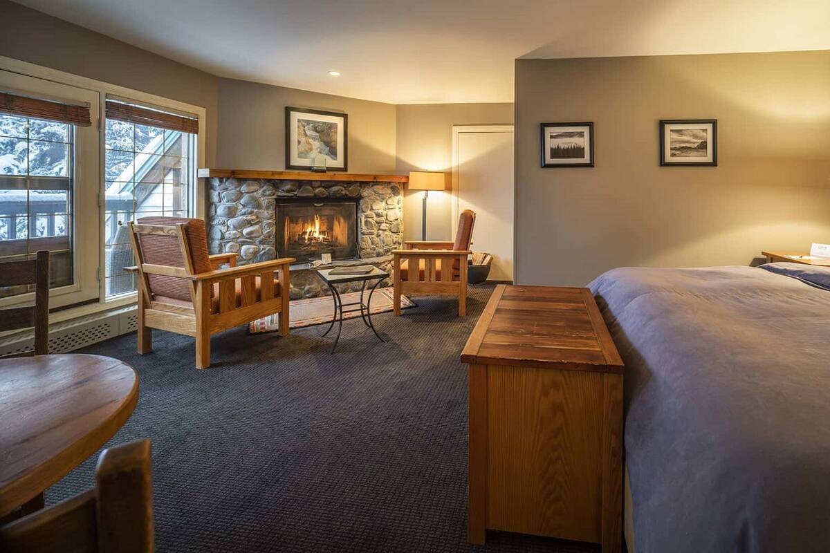 A cozy hotel room with a stone fireplace, a bed, a desk, and a seating area with chairs.