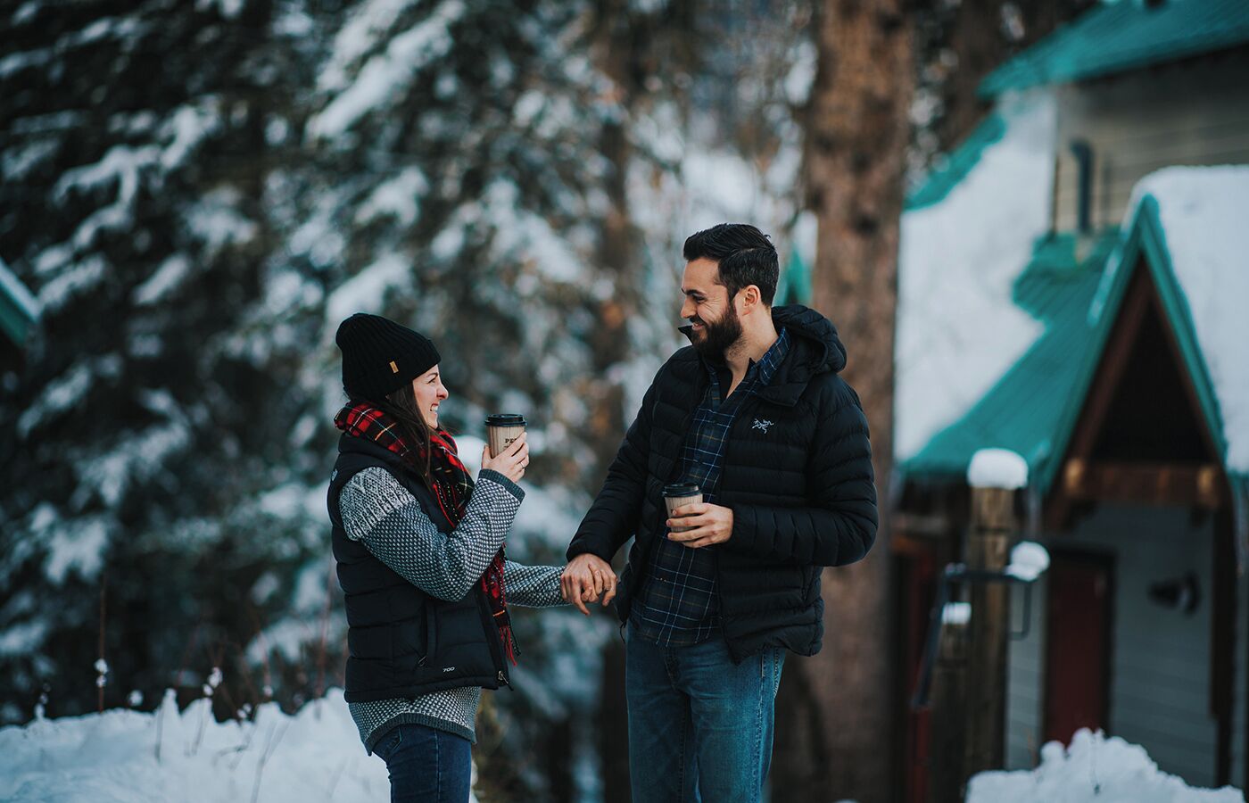 Two people holding hands in a snowy outdoor setting with a building in the background.
