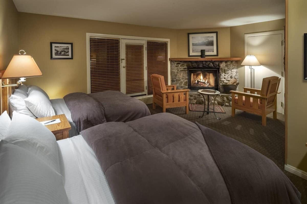 A hotel room with two beds, a fireplace, a small table, and two chairs.