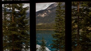 A view through a window of a forested area with a lake and mountains in the background. - Emerald Lake Lodge (Field)