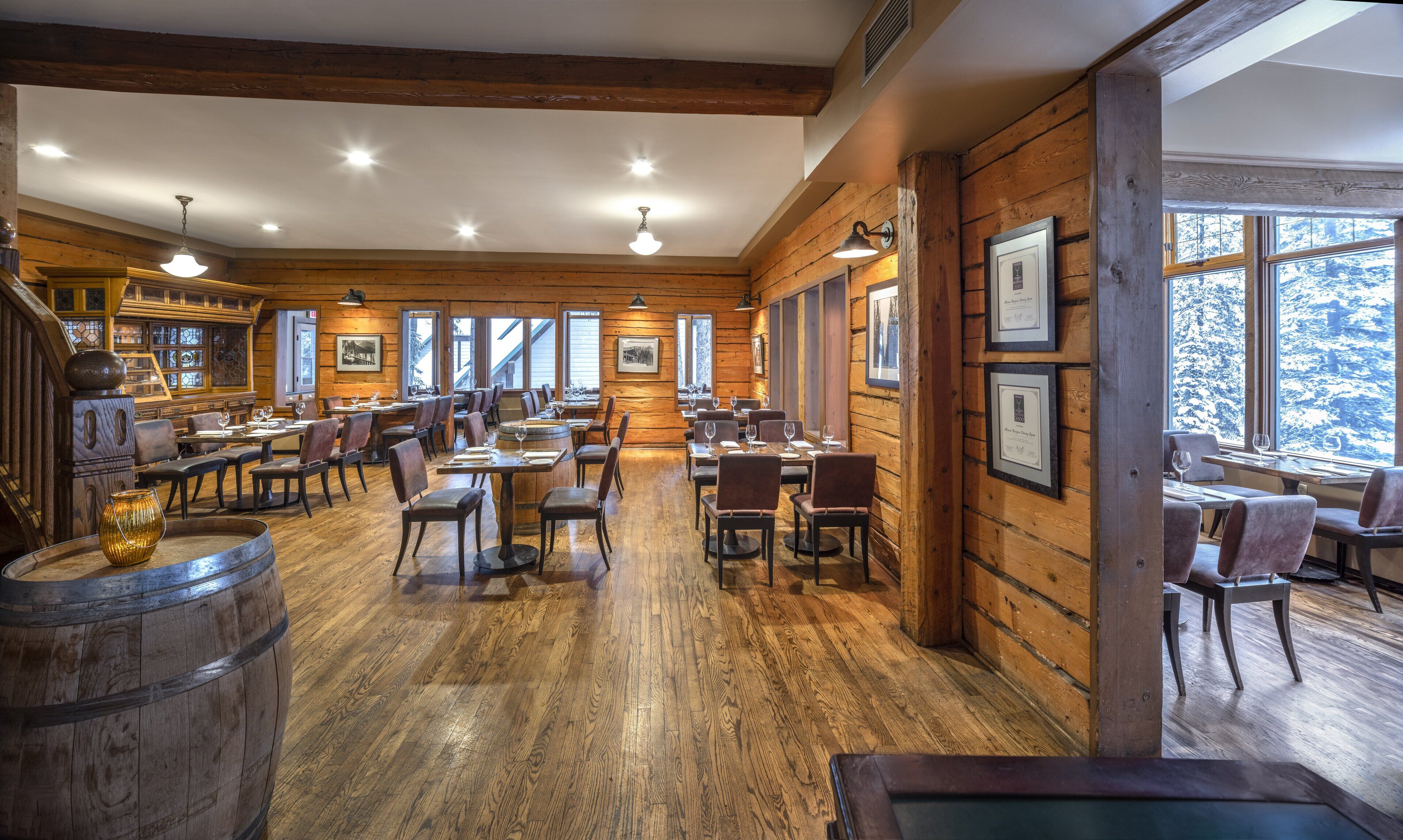 A spacious restaurant with wooden walls and floors, multiple dining tables, and framed pictures on the walls.