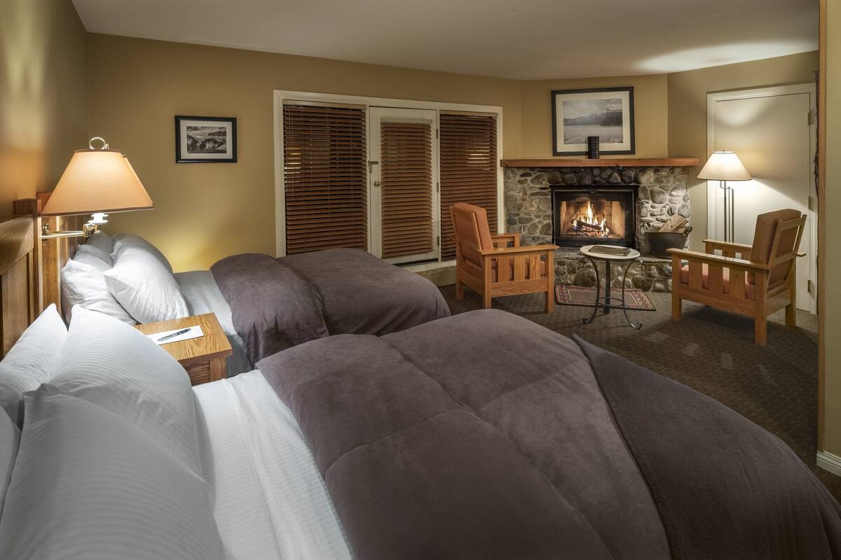 A hotel room with two beds, a fireplace, a small table, and two chairs.