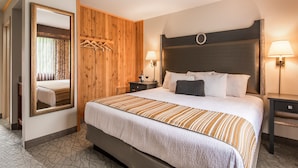 A hotel room with a large bed, wooden panel walls, a mirror, two bedside tables with lamps, and a wardrobe.