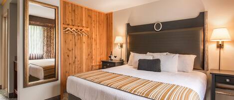 A hotel room with a large bed, wooden panel walls, a mirror, two bedside tables with lamps, and a wardrobe.